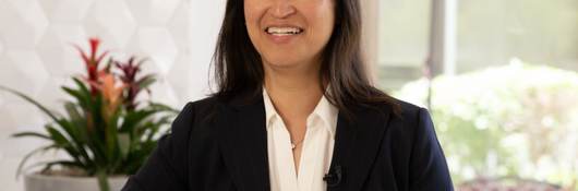 Cynthia Ho in black jacket and white shirt sitting at table. 